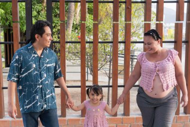 Mutlu İspanyol ailesi, dışarı çıkıp el ele tutuşuyor, hamile anne ve baba ve küçük kızları.