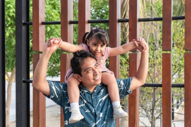 Mutlu İspanyol baba, gülümseyen kızını sırtında taşıyor, parkta birlikte güzel vakit geçiriyorlar.