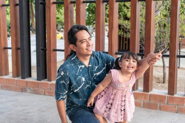 Mutlu İspanyol asıllı adam ve küçük kızı dışarıyı gösterip gülümsüyor.