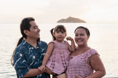 Gülümseyen Aborjinler kızlarını kucağına alıp kumsalda güneşli bir günün tadını çıkarıyorlar.