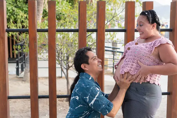 Mutlu İspanyol çift bebek bekliyor, koca karısının karnını tutuyor.