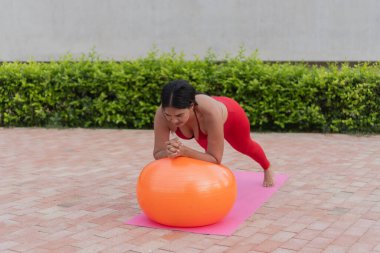 Yoga minderinde turuncu spor topuyla pilates yapan konsantre bayan sporcu.