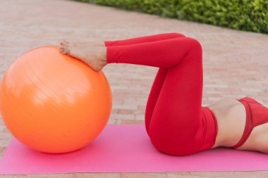 Beden eğitimi hocası pilates egzersizlerini yoga minderiyle dışarıda yapıyor.