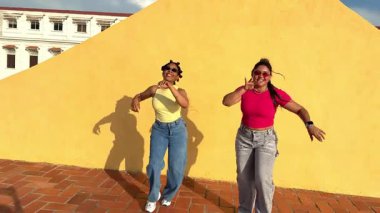 İki kadın dansçı, sarı bir duvarla çatıda dans ediyorlar.