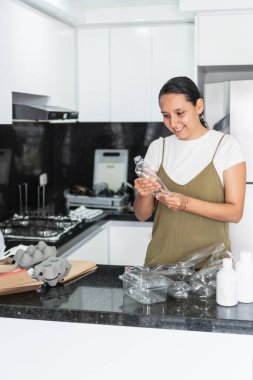 Ev hanımı geri dönüşüm kutusuna koymadan önce plastik şişeyi kontrol ediyor, ev atıklarını sınıflandırıyor ve çevresel sorumlulukları destekliyor