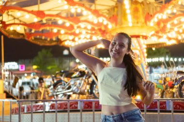 Gülümseyen kadın ışıl ışıl yanan bir atlıkarıncanın önünde poz veriyor