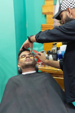 Berber, modern berber dükkanında güzellik tedavisi sırasında rahat müşterilerin kaşlarını tıraş etmek için jilet kullanır.