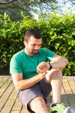 Odaklanmış sporcu, şehir parkındaki antrenmandan sonra akıllı adamı kontrol ediyor.