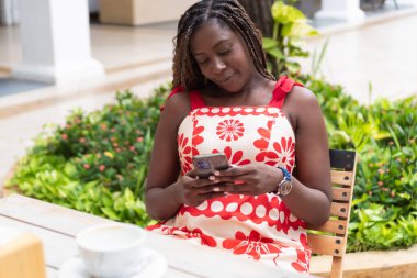 Bir kafede rahatlatıcı bir anın tadını çıkaran mutlu bir müşteri. Yakınlarda bir fincan kahveyle telefonuna göz atıyor.