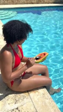 Genç bayan havuz kenarında papaya yiyor.