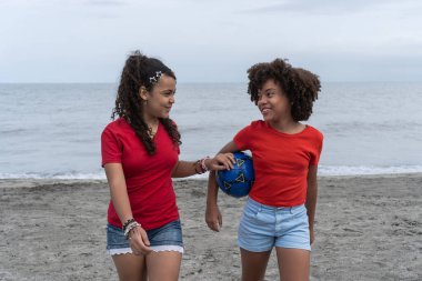 Kumsalda futbol topu tutan iki gülümseyen arkadaş.