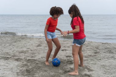 İki farklı kız sahilde futbol oynuyor, eğleniyor ve çocukluğun tadını çıkarıyor.