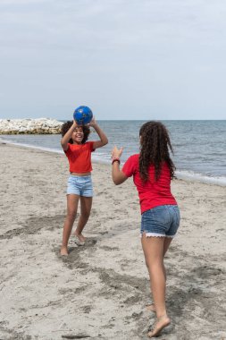 İki arkadaş kumsalda mavi bir topla voleybol oynamaktan hoşlanırlar.