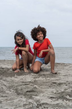 Kumsalda poz veren kıvırcık saçlı iki gülümseyen çocuk.