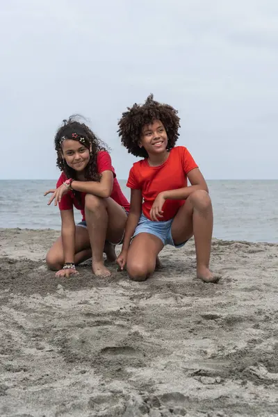 Kumsalda poz veren kıvırcık saçlı iki gülümseyen çocuk.