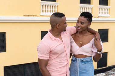 Siyah çift kucaklaşırken gülümsüyor, beraberlik ve sevgi gösteriyor.