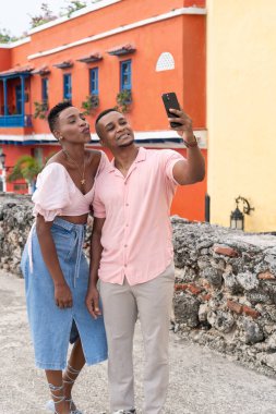Canlı binaların önünde seyahat eden ve selfie çeken siyah bir çift.