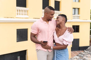 Bir şehir ortamında birbirini kucaklayan ve gülümseyen mutlu siyah çift.