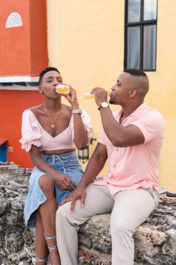 Mutlu siyah çift renkli bir şehirde duvarda otururken içkinin tadını çıkarıyor.