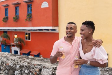 Siyah çift birlikte yürüyor, gülümsüyor ve tatillerinde içki içiyorlar.