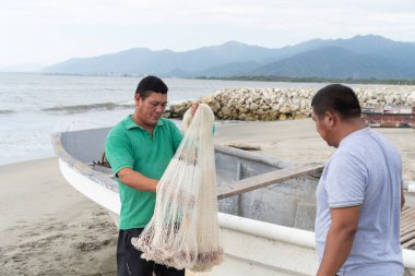 İki balıkçı tekneleriyle kumlu bir sahilde balık ağı hazırlıyor.