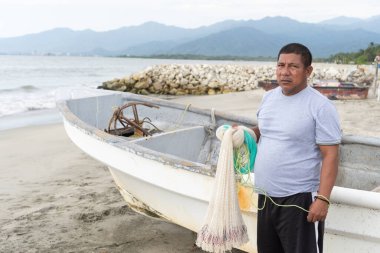Balıkçı, kumlu bir sahilde teknesinin yanında duran alçıdan bir ağ tutuyor.