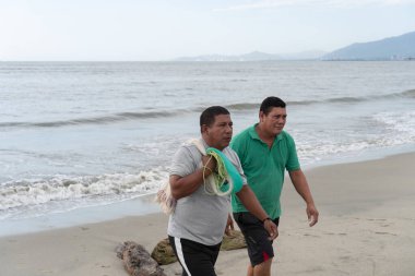 Okyanus kıyısında yürüyen balıkçılar balık ağı taşıyorlar.