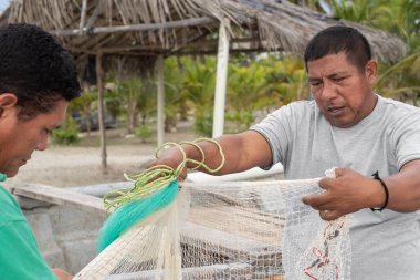 Sahilde çalışan balıkçılar balıkçı ağlarını elleriyle onarıyor.