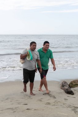 Balıkçılık faaliyetlerinden ağlarıyla dönen iki adam kıyıda yalınayak yürüyor.