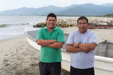 İki İspanyol balıkçı tekneleriyle sahilde kameraya gülümsüyor.