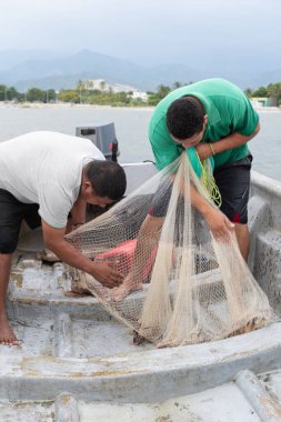 Birlikte çalışan balıkçılar, denizdeki bir tekneden balık ağı çekiyorlar.