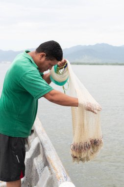 Bir kayıktaki adam suya balık ağı atmaya hazırlanıyor.