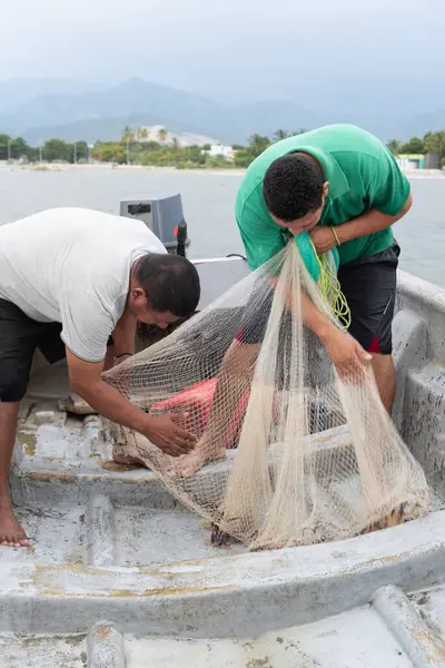 Birlikte çalışan balıkçılar, denizdeki bir tekneden balık ağı çekiyorlar.