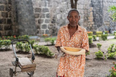 Yaşlı melanezyalı bir adam dışarıda taş duvarlı el yapımı ahşap bir kase sunuyor.