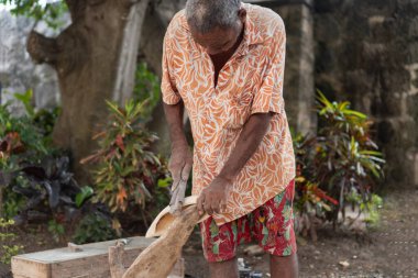 Kıdemli adam dışarıda odun oyuyor, geleneksel zanaat ve konsantrasyon sergiliyor.