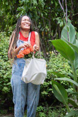 Bir kadın açık havada turuncu gülleri taşırken neşeyle gülüyor.