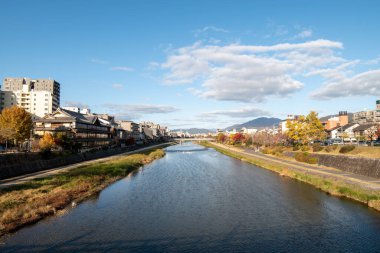 Güneşli bir günde binalar ve kırmızı yapraklarla çevrili sonbahar nehir manzarası (Kyoto, Japonya) (20221208-004)