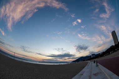 Günbatımında bazı binalar, dağlar ve mavi gökyüzü (Hyogo, Japonya) (20221220-023) olan bir plaj manzarası)