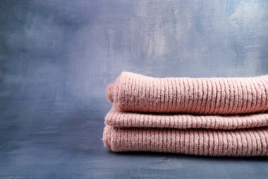 Soft pink wool scarves stacked unevenly on the right, placed on a textured dark blue-grey background. The irregular stack contrasts with the smooth, cool backdrop. clipart