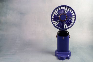Sağdaki küçük mavi vantilatör, dokusu gri arka planda. Boyutunu ve işlevselliğini vurgulayan ince detaylarla basit, minimal tasarım.