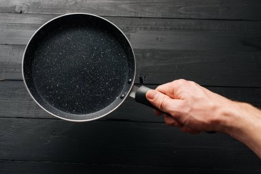 Eldeki boş tava siyah ahşap arka planda.