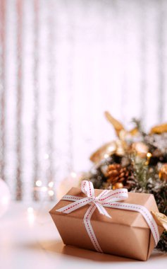 Kraft karton hediye kutusu. Gri ahşap arka planda kaba halatla bağlanmış. Noel ağacı dalları ve Noel süslemeleri var..