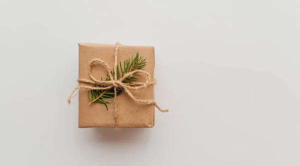 stock image Kraft cardboard gift box tied with rough jute rope on gray wooden background with branches of Christmas tree and Christmas decorations.