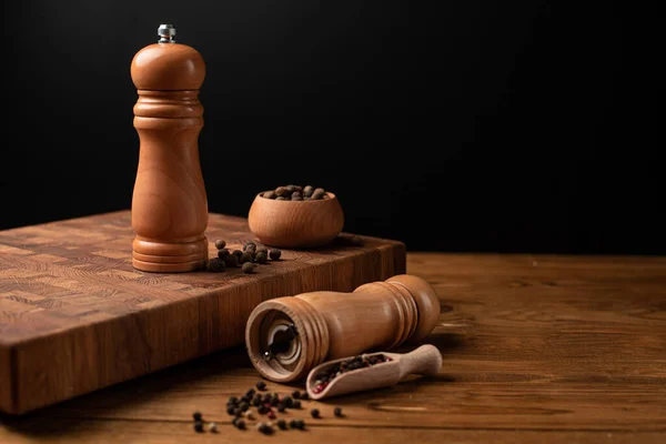 Pepper mill and whole pepper in wooden scoop on black table. Top view