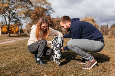 Genç bir çift açık havada Dalmaçyalı bir köpekle eğleniyor.