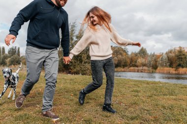 Genç bir çift açık havada Dalmaçyalı bir köpekle eğleniyor.