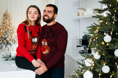 Mutlu çift hediye kutuları ve noel ağacının yanında. Birbirlerine sarılıp Noel ağacının yanında birbirlerine bakıyorlar.