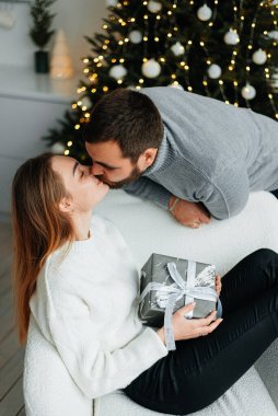 Mutlu çift hediye kutuları ve noel ağacının yanında. Birbirlerine sarılıp Noel ağacının yanında birbirlerine bakıyorlar.