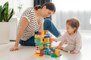 Gülen anne ve küçük kız renkli bloklar yapıyor, kule inşa ediyor, yer altı ısıtmalı sıcak zeminde oturuyor, aile birlikte vakit geçiriyor..