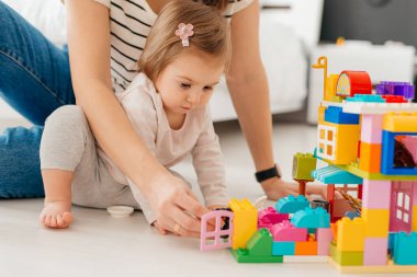Gülen anne ve küçük kız renkli bloklar yapıyor, kule inşa ediyor, yer altı ısıtmalı sıcak zeminde oturuyor, aile birlikte vakit geçiriyor..